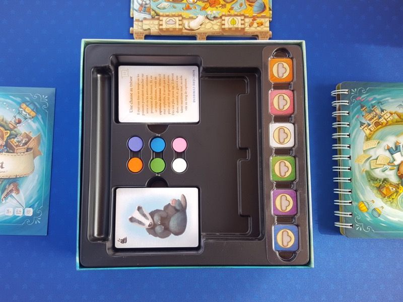 2 paquets de cartes sous blister, 6 pions en bois, des jetons de couleurs (orange, rose, blanc, vert, violet et bleu).