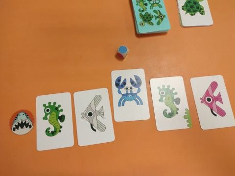 Après avoir placé sa carte, le joueur lance le dé Attaque : si le dé tombe sur une face couleur (ici le bleu)  alors il doit choisir une de ses cartes de cette couleur (si présente devant lui) et la mettre face visible dans la défausse.