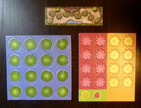 La piste de score, les jetons nénuphars, les jetons fleurs rouges, les jetons fleurs jaunes et les 2 pions grenouilles.