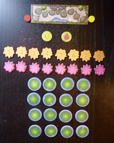 La piste de score avec les 2 pions jardiniers, les 2 grenouilles, les 8 jetons nénuphars numérotés de 1 à 8 dans chaque couleur et les 16 jetons nénuphars le tout dans du carton bien épais.