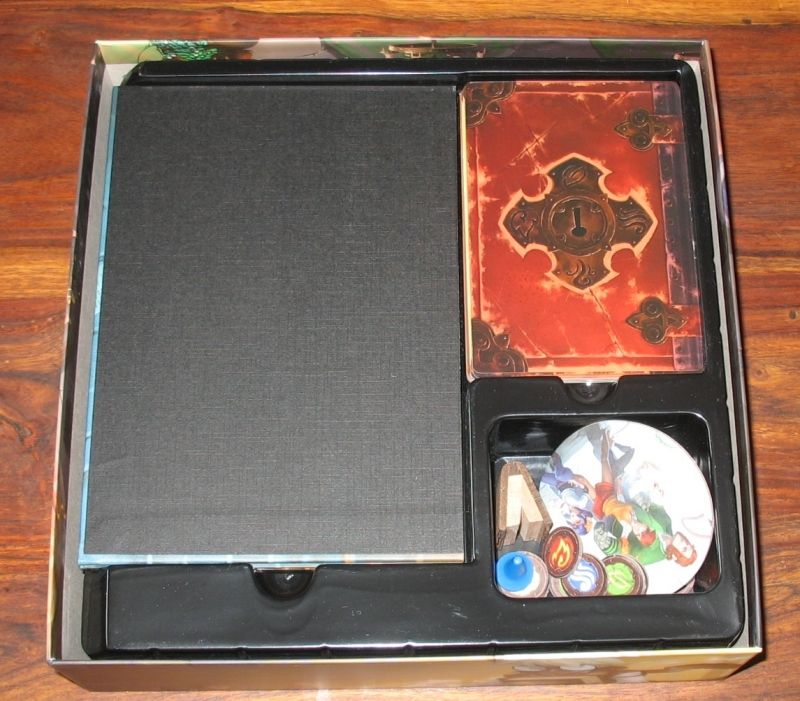 On aperçoit le plateau plié en quatre, les cartes grimoire et des jetons.